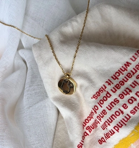 Détail du collier à pendentif rond doré avec dessin au trait minimaliste de visage