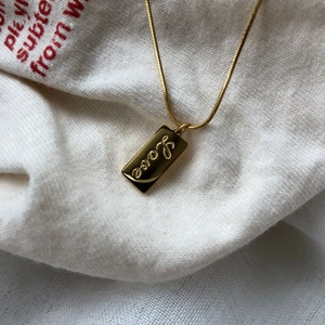 Macro detail of 18K gold snake chain with a rectangular LOVE engraved pendant charm