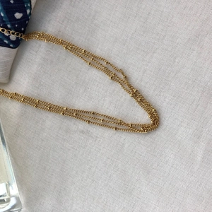 Three-layer vintage gold beaded necklace in titanium steel on a white fabric background
