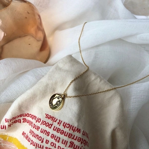 Vue détaillée d'un collier à pendentif rond doré avec une gravure de visage abstrait