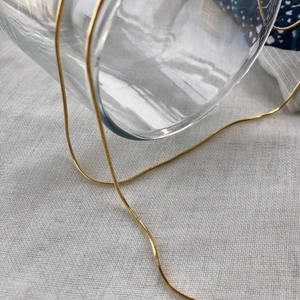 Collier élégant en maille serpent dorée sur lin blanc au design minimaliste chic