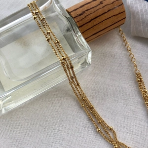Close-up of a three-layer gold beaded necklace wrapped around a glass perfume bottle