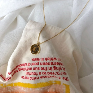 Détail d'un collier doré avec un pendentif rond gravé d'un visage abstrait de style moderne