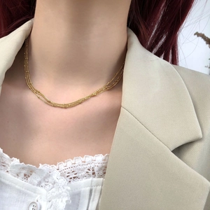 Detail of layered gold beaded chain necklaces worn with a beige blazer for elegant styling