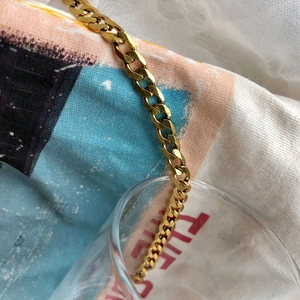 Bracelet chaîne cubaine dorée polie présenté sur un fond lifestyle artistique