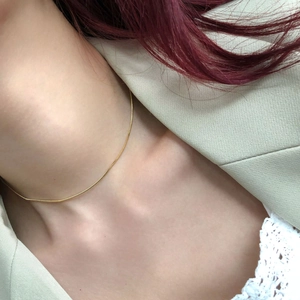 Gros plan d'un collier chaîne serpent dorée minimaliste porté sur la clavicule