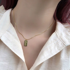 Detail of 18K gold-plated necklace with a vertical square Love tag on a model's collarbone