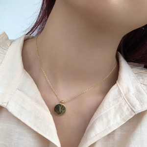 Gros plan d'un collier doré minimaliste avec pendentif circulaire au visage abstrait