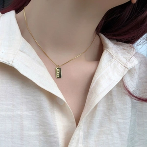 Detail of 18K gold rectangular pendant necklace with Love engraving on a female neck