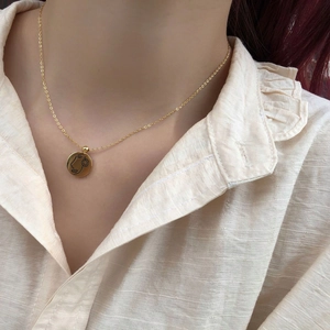 Gros plan d'un collier à pendentif rond doré avec gravure minimaliste de visage féminin