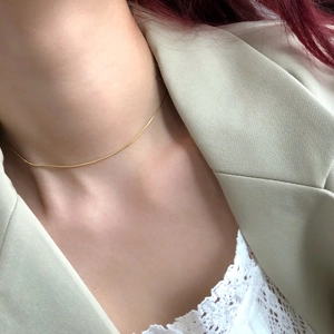 Détail macro du collier ras du cou doré à maille serpent minimaliste sur le décolleté