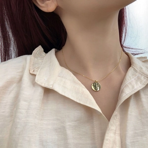 Gros plan d'un collier doré avec pendentif visage minimaliste porté sur la clavicule