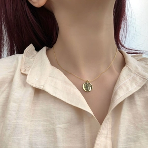 Détail d'un collier en or avec gravure de visage abstrait porté par un mannequin