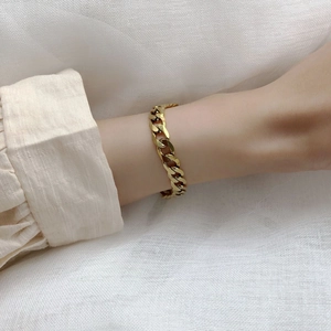 Gros plan d'un bracelet gourmette doré épais au poignet sur un fond en lin texturé doux