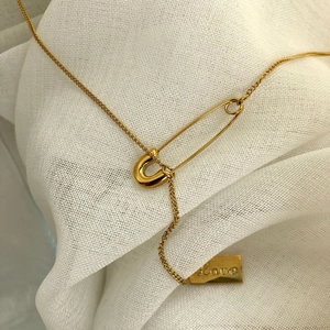 Minimalist gold safety pin necklace with engraved Love plaque on textured fabric