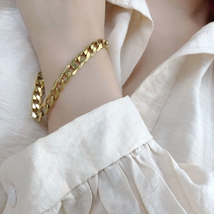 Bracelet gourmette épais en acier titane doré porté sur une manche de chemise beige crème