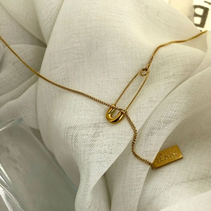 Minimalist gold pin necklace with Love engraved rectangular plaque on white fabric