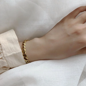 Vue détaillée d'un bracelet gourmette doré à gros maillons au poignet d'une femme à volants