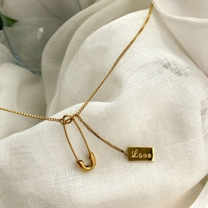 Close-up of gold safety pin and Love square tag pendants on a delicate chain necklace