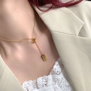 Minimalist gold pin and Love tag necklace on model in elegant beige suit attire