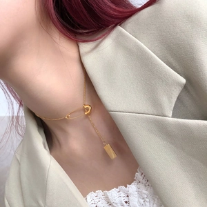 Detail of gold safety pin necklace with rectangular pendant worn over a beige blazer