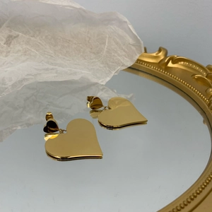 Elegant gold layered heart earrings with polished finish displayed on a mirror surface