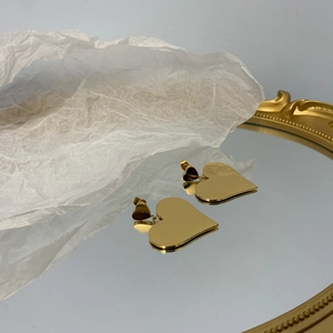 Detail of glossy gold heart-shaped drop earrings with double heart design on white paper
