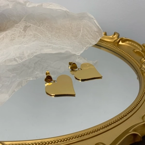 Detailed macro view of polished gold-tone metal heart drop earrings on a mirror surface
