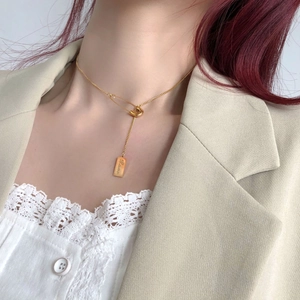 Detail of gold safety pin necklace with Love rectangular pendant on a model in a beige suit