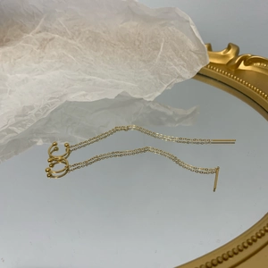 Detail shot of golden long chain tassel earrings with ear cuff on a mirror surface