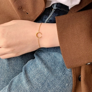 Dettaglio di un bracciale a mezzaluna dorato al polso con un elegante outfit in stile francese
