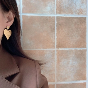 Modern dual heart gold drop earrings for women with a matte finish worn by a model