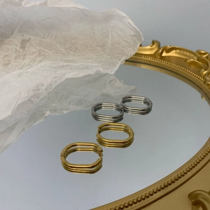 Close-up of geometric oval hoop earrings in gold and silver finish on a mirror tray