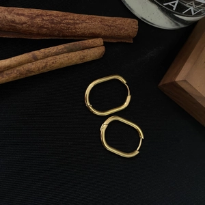 Close-up of geometric oval gold earrings with a polished finish on black fabric