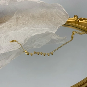 Dettaglio di un bracciale dorato a doppia catena con piccoli pendenti tondi in metallo