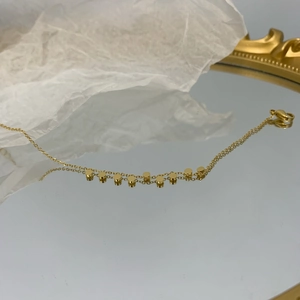 Dettaglio di catena con ciondoli a disco dorati e chiusura a moschettone su uno specchio