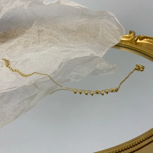 Dettaglio di una collana dorata con piccoli ciondoli a disco tondi posati su uno specchio