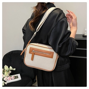 Dettaglio borsa a tracolla in tela beige con finiture in pelle marrone e tracolla larga