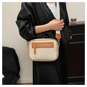 Dettaglio di una borsa a tracolla in tela beige e pelle marrone indossata da una modella