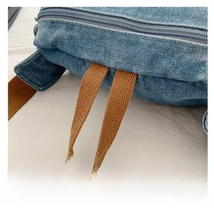 Détail d'un sac bandoulière en denim bleu avec poignée tissée marron et fermeture éclair