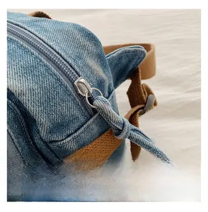 Détail de la fermeture éclair argentée et du denim bleu avec sangle brune du sac