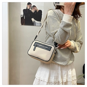Dettaglio borsa a tracolla quadrata in tela beige con finiture nere e cinghia