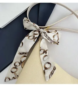 Detail of elegant beige handbag strap with silk scarf and gold metal buckle accents