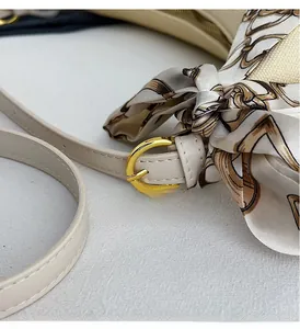 Detail of beige shoulder bag featuring adjustable strap with gold buckle and silk scarf