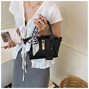 Close-up of black woven bucket bag with gold lock, silk scarf handle and logo tag