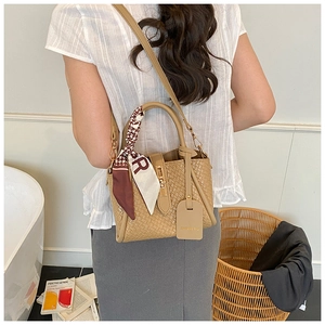 Close-up of beige woven bucket bag with twist lock and decorative silk scarf detail