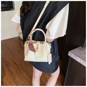 Detail of cream woven bucket bag with gold lock, decorative scarf, and adjustable strap