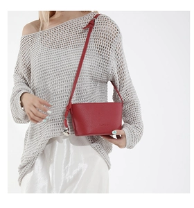 Detail of red faux leather crossbody bag with FASHION embossed logo and silver charm