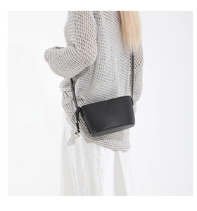 Detail of a black lychee grain leather crossbody bag with a silver heart pendant on model