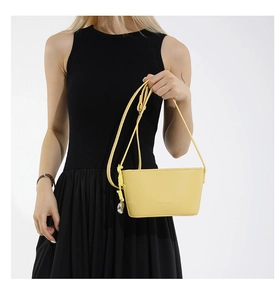 Detail of bright yellow leather crossbody bucket bag with textured finish and woven charm